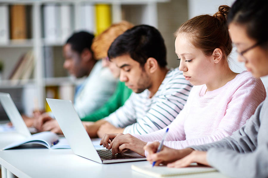 Male and female students writing and working on laptops