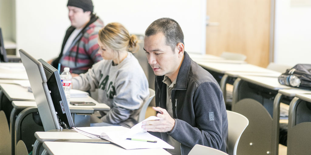 three students working working in class, one with a computer