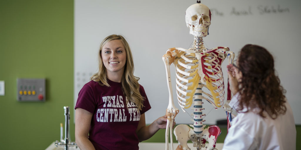A student and an instructer standing near a human skeletal model
