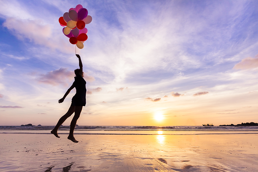 person jumping in the air, over water, with balloons in hand