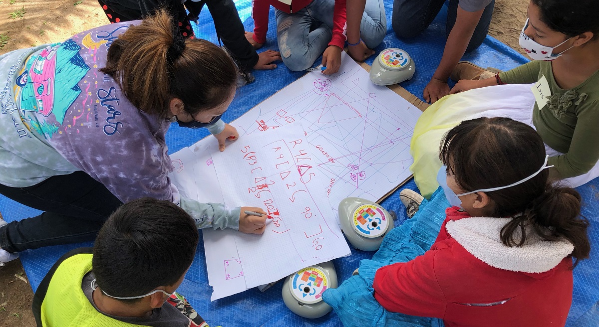 students and a teachers kneel around a programmable floor robot