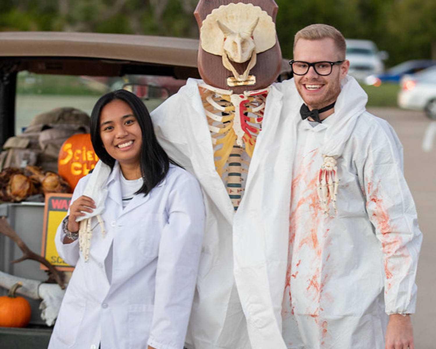 students dressed in mad scientist costumes stand next to a skeleton