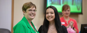 Two women smiling for the camera, one in a bright green blazer, the other in a black dress.