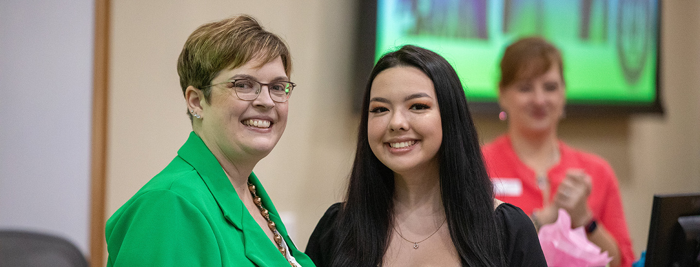 Two women smiling for the camera, one in a bright green blazer, the other in a black dress.