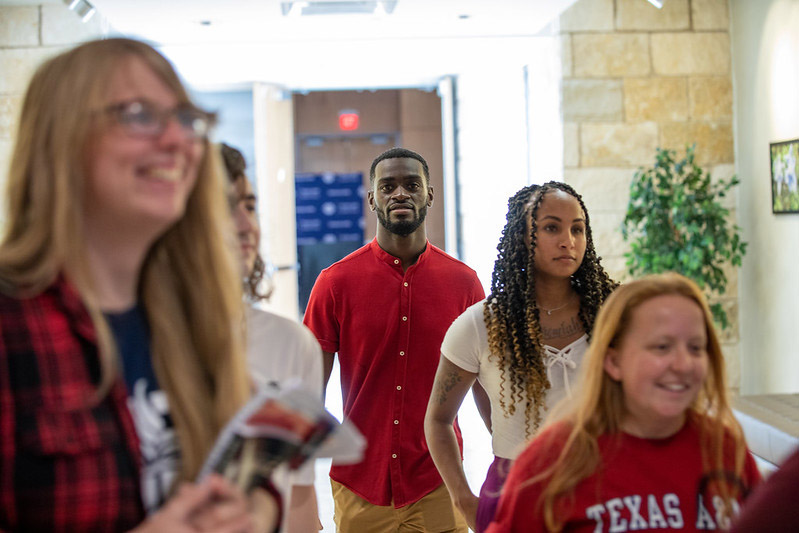 A collection of five A&M-Central Texas students standing in a hallway, focused on something or someone.