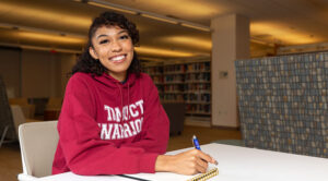 Summer Velasco sitting in a library, with a pen and notebook on her desk