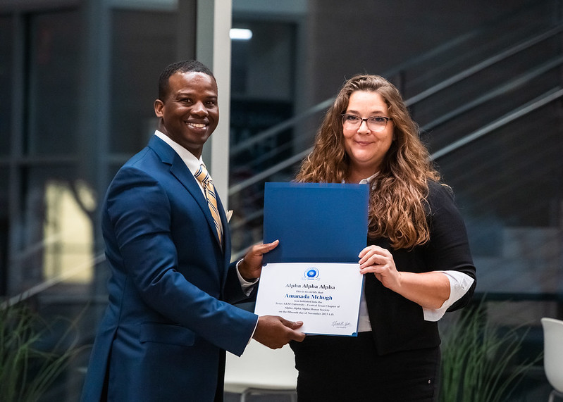 A man presents Amanda McHugh with a certificate for Tri Alpha.