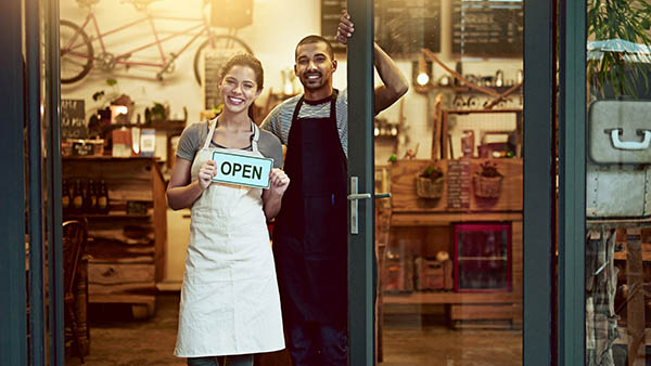 A man and woman holding up an open sign for their store.