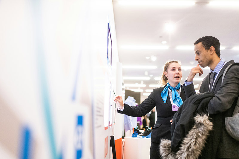 A businesswoman and businessman deliberate something in front of a board that is covered in papers