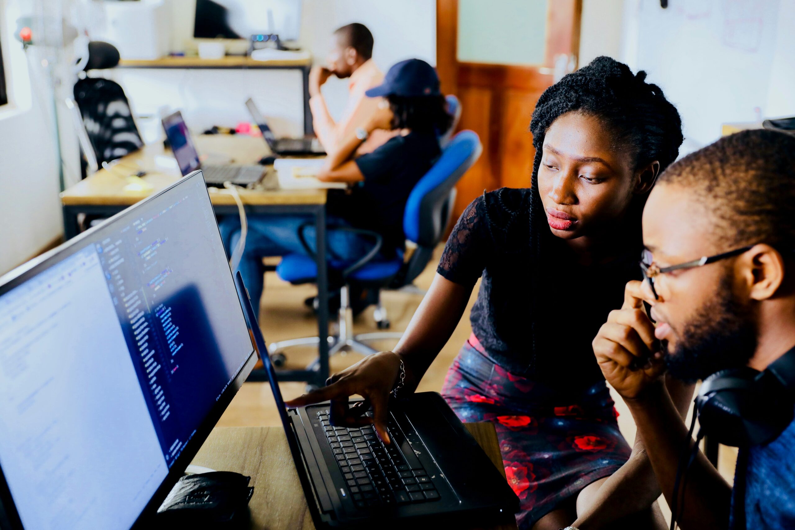 A woman helps a man, showing him something on a laptop