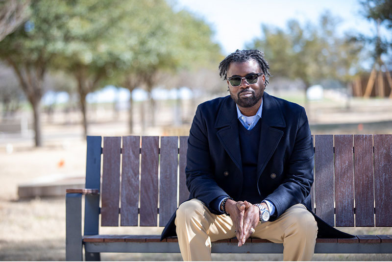 Assistant Professor of Accounting Dr. Anthony Fulmore, sitting on a bench in a park while wearing sunglasses.