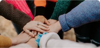 A collection of people putting their hands together in the middle of their circle.
