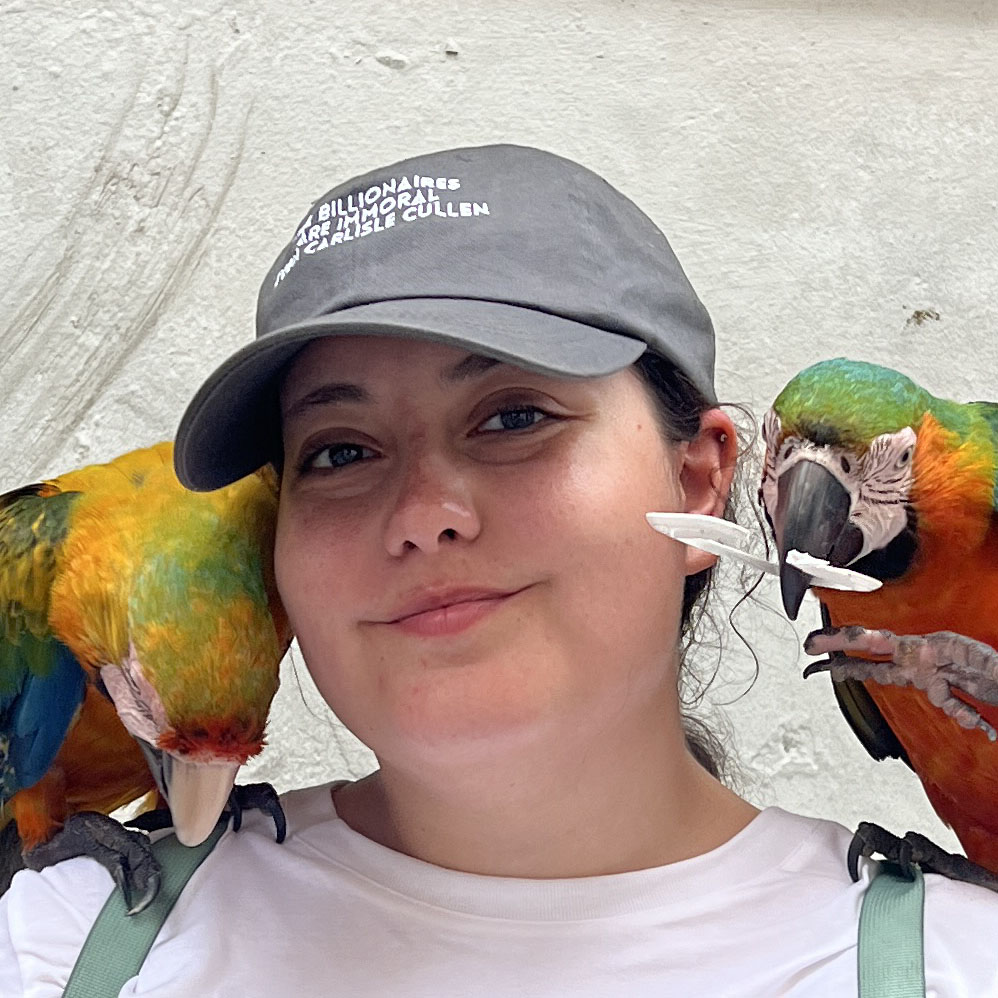 A selfie of Texas A&M University-Central Texas student Laura Montero, as she smiles at the camera with two colorful birds on her shoulders.