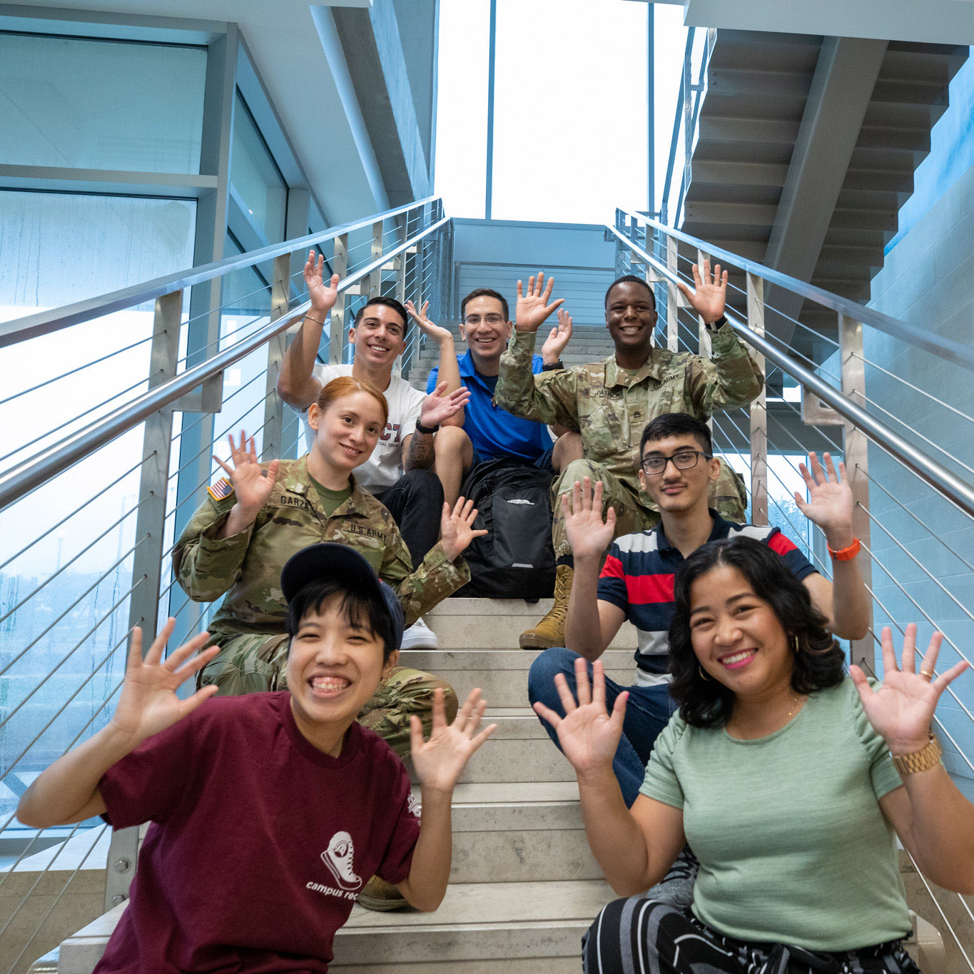 Seven students sitting on a staircase, grinning with their hands in front of them.
