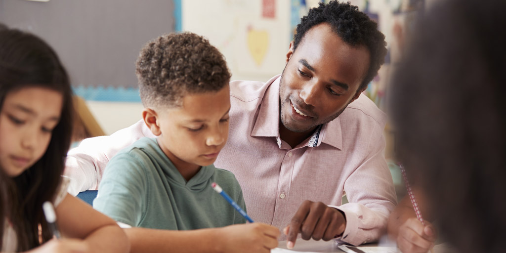 A man helps a young boy who is writing on a paper.
