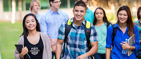 young adults walking outdoors on school campus. Students are smiling while walking together to class. 