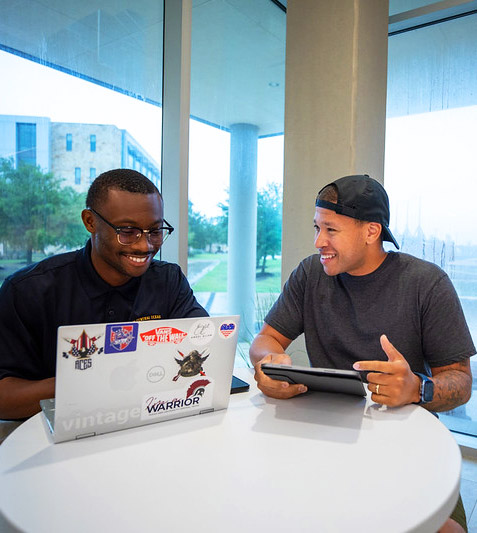 Two Community College students sitting at a table together with devices