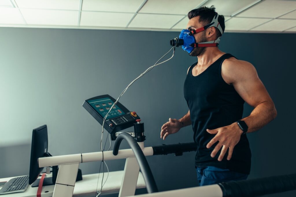 Fitness man running on treadmill with a mask testing his performance. Athlete examining his performance in sports science lab.