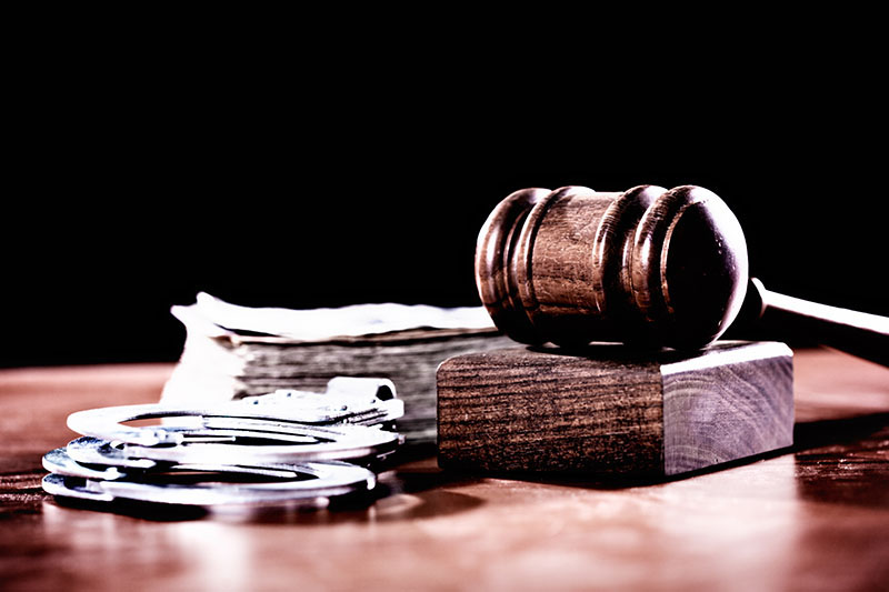 A wooden judge's gavel with a stack of banknotes, possibly symbolising  bribery and problems in the justice system, plus a pair of handcuffs, symbolising crime.