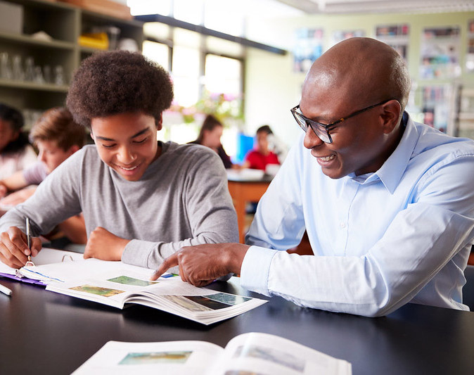 A man tutoring a boy in a classroom