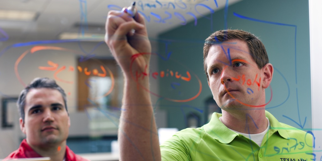 A man writes on a clear dry erase board