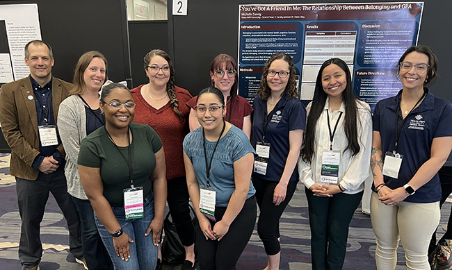 Psychology students and faculty coordinators smile in front of a reseach poster.