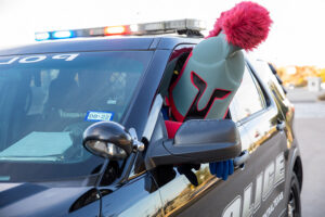 Pathfinder mascot in the driver's seat of a TAMUCT police car and poking his head outside of the window.