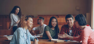Photo of university students discussing classwork, with textbooks and notepads.