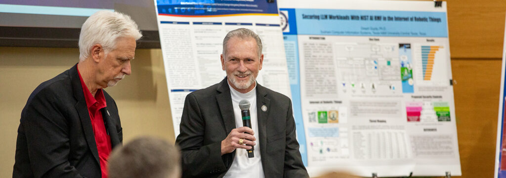 Dr. Rhodes sitting in front of a group, one is holding a microphone and talking.