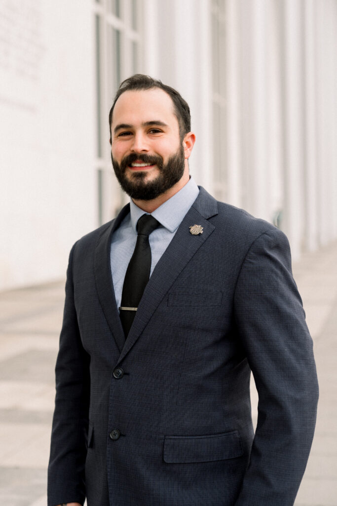 Portrait of a young man with short hair and full beard in a coat and tie.