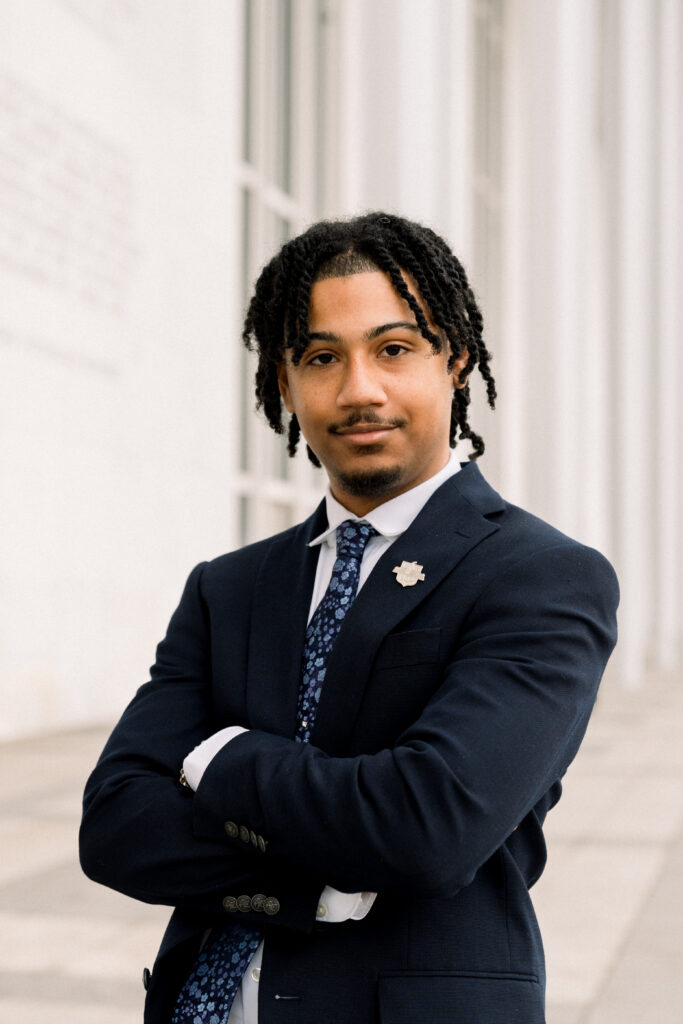 Portrait of a young man with braided hair and goatee and mustache.