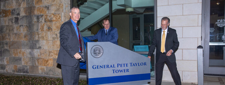 Three men unveil the General Pete Taylor Tower sign.