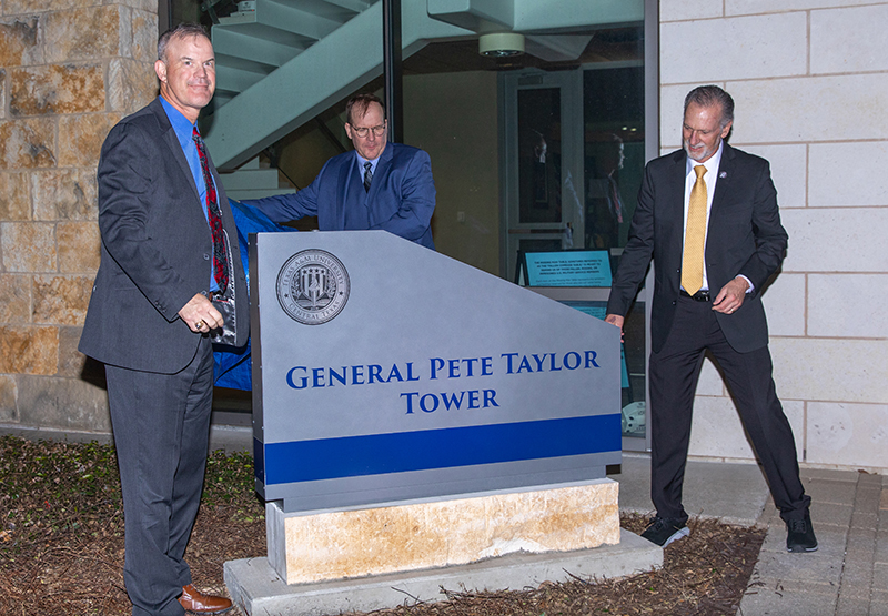 Three men unveil the General Pete Taylor Tower sign.