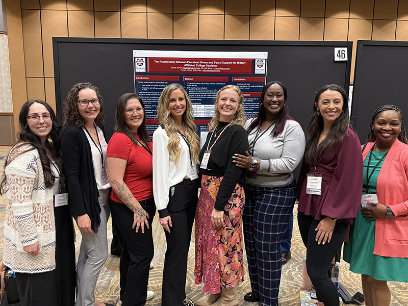 A group of 8 women lined up in front of an academic research poster.