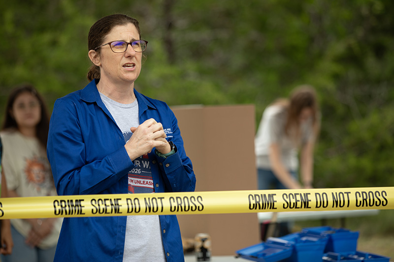 A woman standing behind crime scene tape with hands clasped talking. 