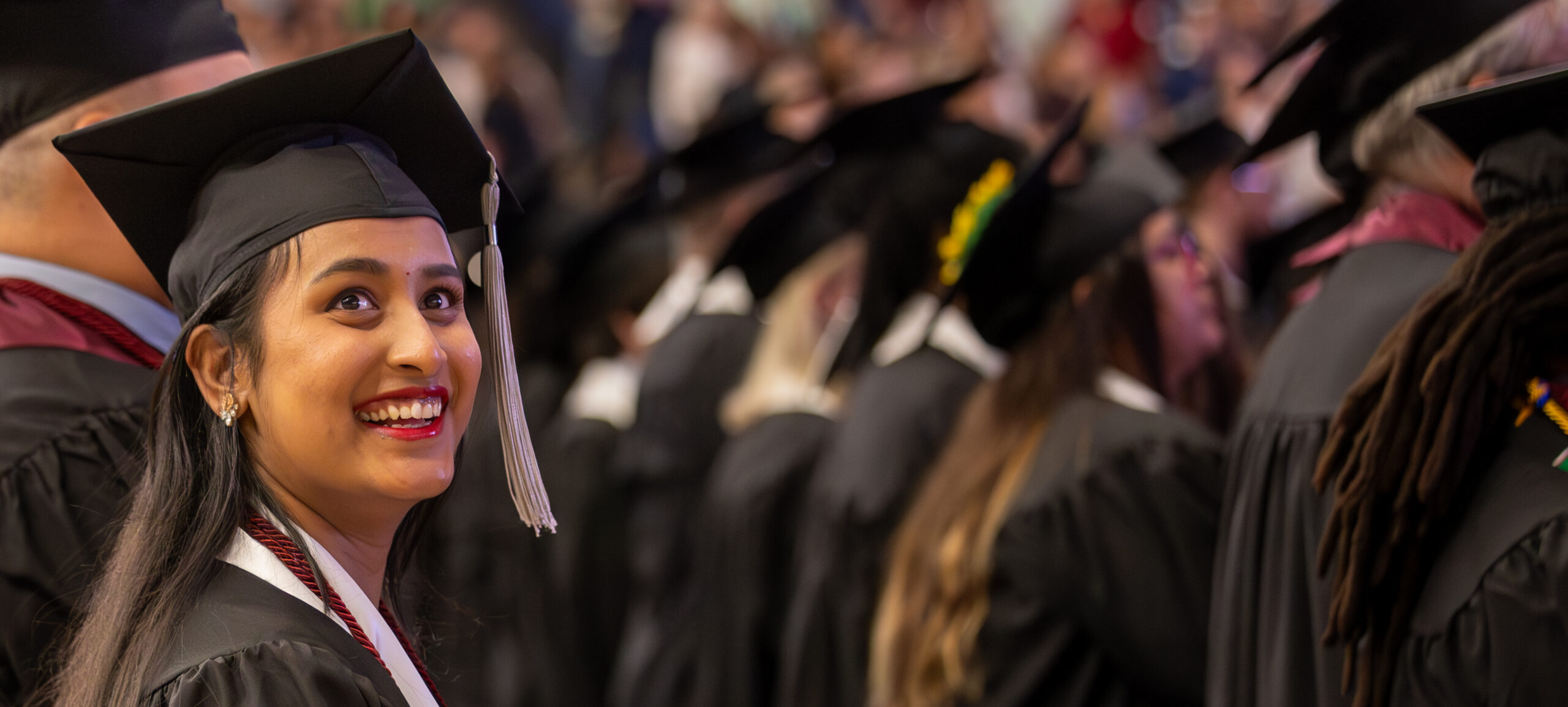 A graduate stands with other graduates and smiles at the stands