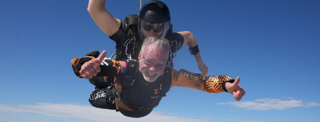 75 year old man gives a thumbs up as he free-falls during a tandem skydiving jump.