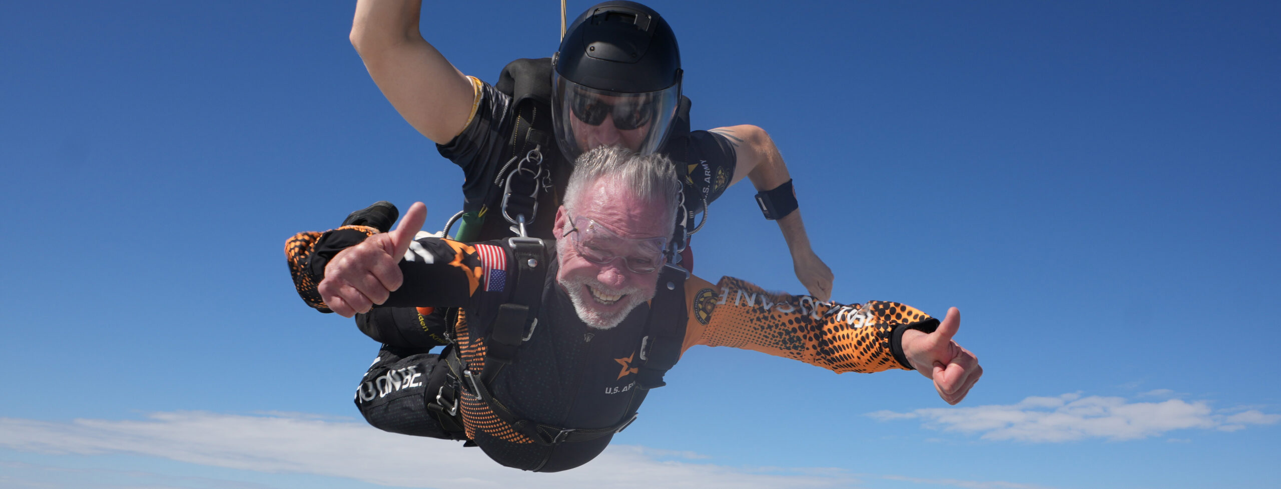 75 year old man gives a thumbs up as he free-falls during a tandem skydiving jump.