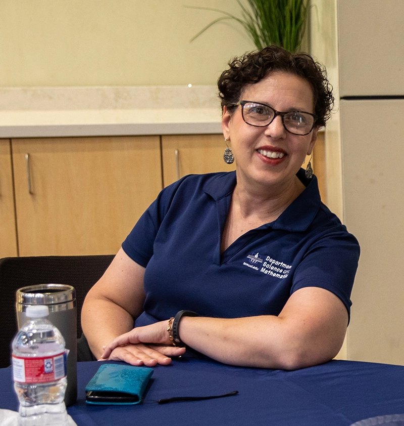 Dr. Laura Erlandson poses for a photo while sitting at a table wearing glasses and blue polo shirt.