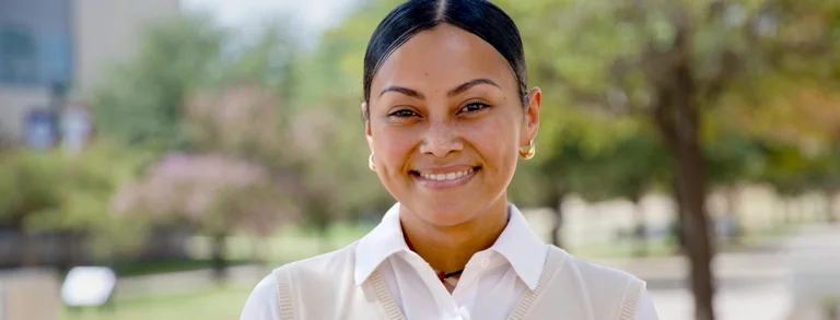 Young woman, Nadine Tochi, smiling at the camera wearing a white blouse and sweater vest.