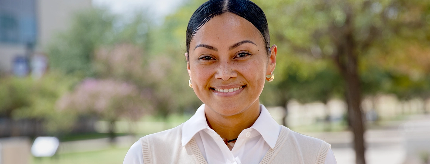 Young woman, Nadine Tochi, smiling at the camera wearing a white blouse and sweater vest.