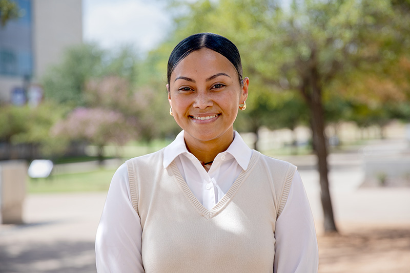 Young woman, Nadine Tochi, smiling at the camera wearing a white blouse and sweater vest.