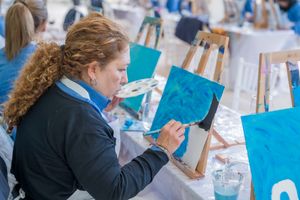 An adult woman engaged in a painting session at an art workshop with easels and paint.
