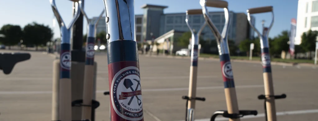 Close up of shovel handles leaning on stands with university buildings in the background.