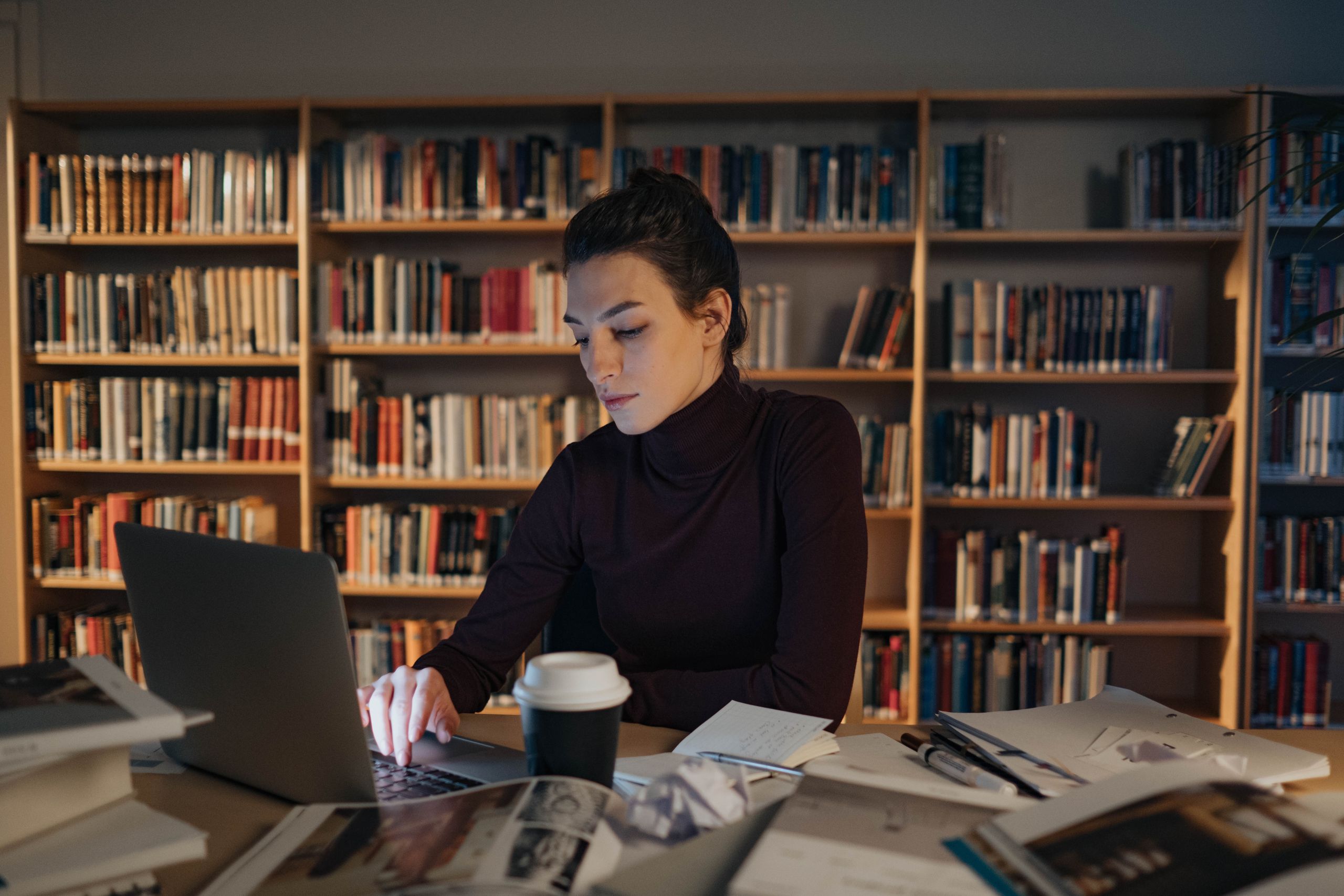 Adult woman intensely focused while working on a laptop in a library setting.