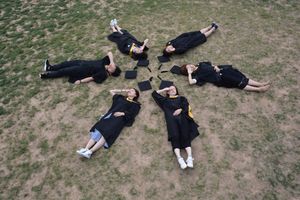 Overhead view of six graduates lying in circle on grass, celebrating.