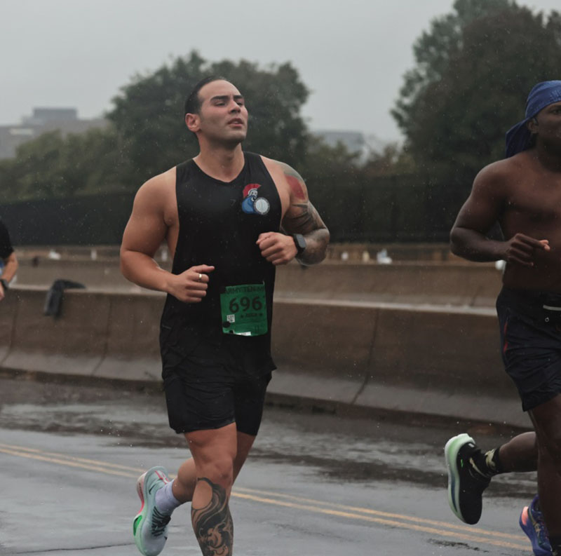 Man in black shorts and tank top running in the rain.
