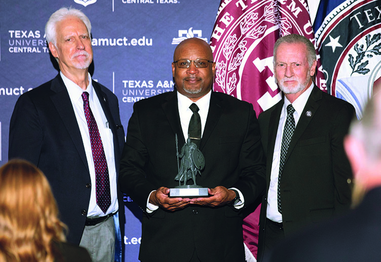 Three men in a row. The center man is holding a Warrior statue.